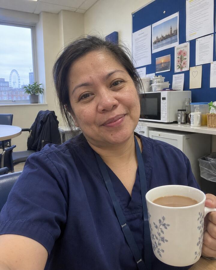 Selfie of Tolu in navy scrubs holding a mug of tea